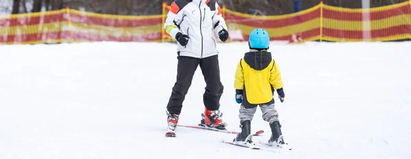 Instruktor i małe dziecko na nartach. Dzieciak w kasku. Lekcja narciarstwa dla małych dzieci. Zimowy sport. Mały narciarz. — Zdjęcie stockowe