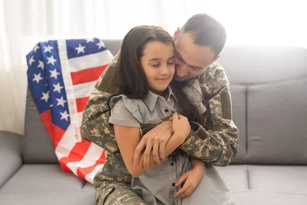 Retrato de feliz pai da família americana em uniforme militar e filha menina bonito com bandeira dos Estados Unidos abraçando e sorrindo para a câmera — Fotografia de Stock