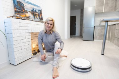 Yerleri temizlemek için otomatik süpürge kullanan genç bir kadın.