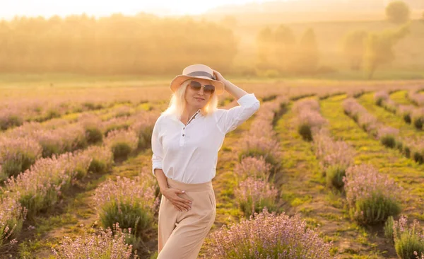 美しい若い健康な女性白いドレスは、夕日の光の下でわら帽子を保持ラベンダー畑を楽しく実行しています — ストック写真