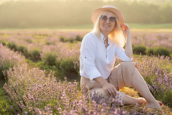 若いブロンドの女性旅行者はラベンダーの花で囲まれたラベンダー畑でわら帽子をかぶって. — ストック写真