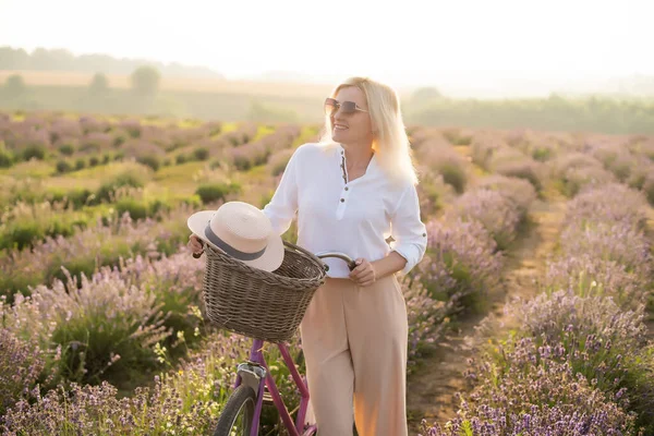 若いブロンドの女性旅行者はラベンダーの花で囲まれたラベンダー畑でわら帽子をかぶって. — ストック写真