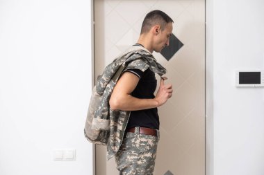 Kamuflajlı asker evin kapısında dikiliyor.