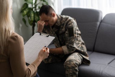 Psikologla terapi seansı sırasında koltukta oturan depresif bir asker.