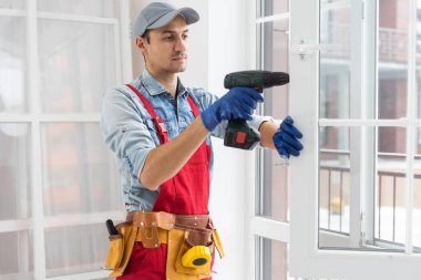 Yakışıklı genç adam yeni bir inşaat alanına pencere takıyor..