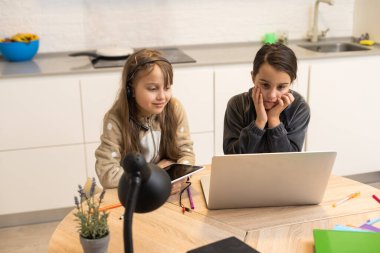 Online eğitim. Kulaklıklı iki liseli kız kardeş dizüstü bilgisayarlardan ders dinliyorlar. Okulda salgın ve karantina var..