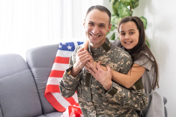 Retrato de feliz pai da família americana em uniforme militar e filha menina bonito com bandeira dos Estados Unidos abraçando e sorrindo para a câmera — Fotografia de Stock