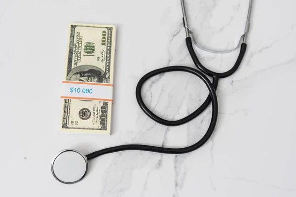 Vård, försäkring och ekonomi koncept: Amerikanska hundra dollar sedlar med ett stetoskop ovanpå det ligger på svart bakgrund. Regeringar som omfattar vaccinering mot covid-19-pandemi. — Stockfoto