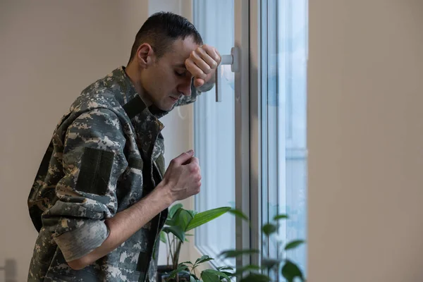 Soldado deprimido y triste en uniforme verde con trauma después de la guerra de pie cerca de la ventana —  Fotos de Stock