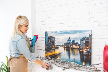 Mutlu ev hanımı kameraya gülümsüyor. Elinde bez ve sprey şişeyle.