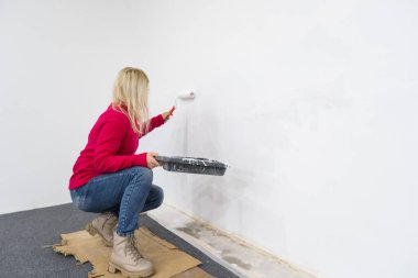 Kapatın. Kafkasyalı güzel bir kadının tek başına yeni evde yeşil renge boyadığı bir manzara. Güzel bir kadın evi yeniliyor. Duvarı paten fırçasıyla boyuyor. Daireyi yeniden tasarlıyor.