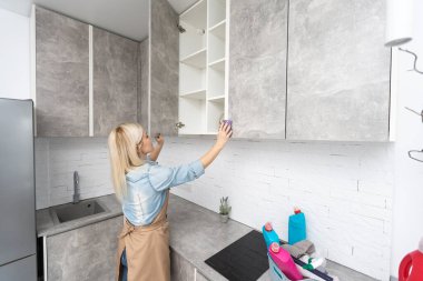 İnsanlar, ev işleri ve ev işleri konsepti. Evde mutfağı süngerle temizleyen bir şişe sprey ile sarışın orta yaşlı kadın..