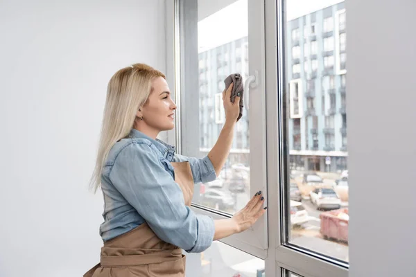 Mujer sonriente joven lavando ventana con esponja. Ventana de limpieza Happy Beautiful Girl rociando productos de limpieza y limpiando con esponja. Casa de limpieza mujer —  Fotos de Stock