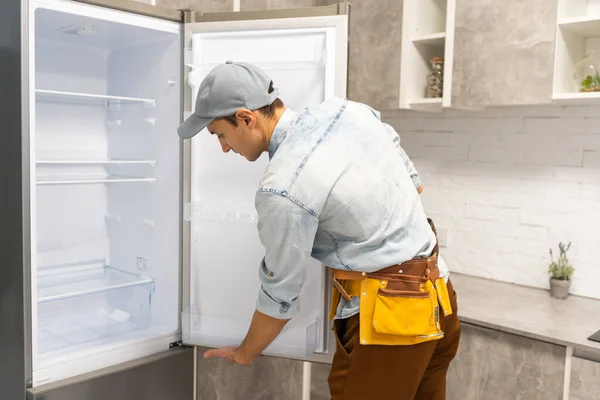 Artesão adulto em trabalhar a escrita geral na área de transferência perto do refrigerador quebrado na cozinha — Fotografia de Stock