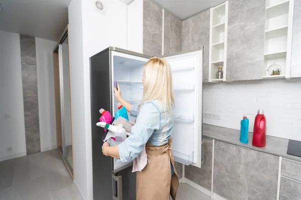 Jovem sorrindo profissional serviço de limpeza mulher limpeza geladeira na cozinha — Fotografia de Stock