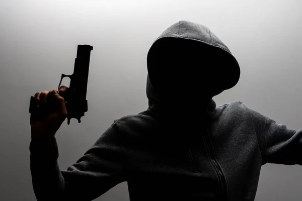 Foto eines gruseligen Horror-Verbrechers in schwarzem Kapuzenpulli mit Revolverpistole. — Stockfoto