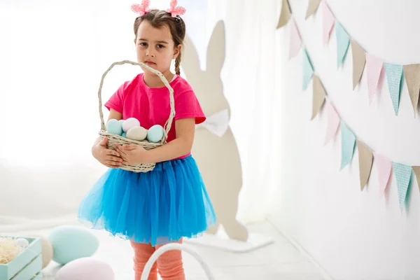 Getting ready to Easter. Lovely little girl holding an Easter egg and smiling with decoration in the background — Stock Photo, Image