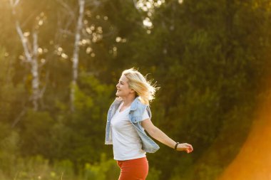 Çekici genç bir kadın, arka planda günbatımıyla parkta eğleniyor..