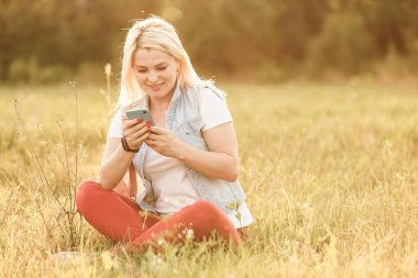 Şirin bir kadın parkta otururken cep telefonundan hoş bir mesaj okuyor, muhteşem bir kadın müzik dinliyor ve cep telefonundan bilgi topluyor.