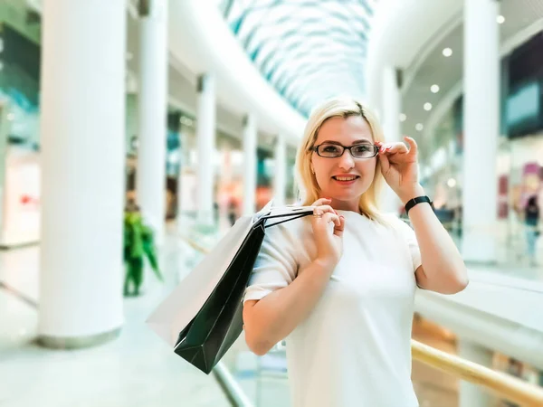 美丽而快乐的女孩，戴着眼镜，手里拿着袋子，在城里购物. — 图库照片