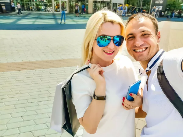 Birlikte alışveriş. Akıllı telefonu açık havada kullanan mutlu çift, alışveriş merkezinin yakınında yürüyor — Stok fotoğraf
