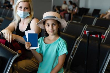 Yüzü maskeli bir anne ve kız tatilde, havaalanında.