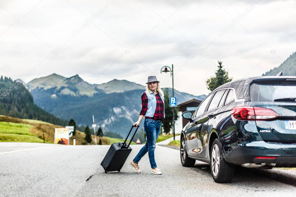 Woman with car near countryside road through mountain Alps