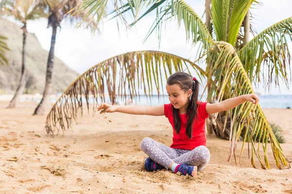 Маленькая милая девочка играет на пляже рядом с пальмой. — стоковое фото