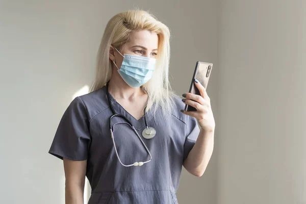 El doctor se toma selfies por teléfono. Enfermera vistiendo un traje con un teléfono en las manos. — Foto de Stock