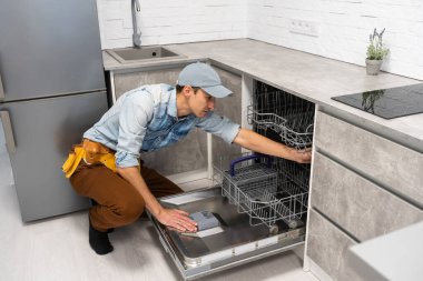 Genç yetişkin adam boşalıyor, yükleniyor. Ev işleri, modern mutfak gereçleri. Açık bir bulaşık makinesi.