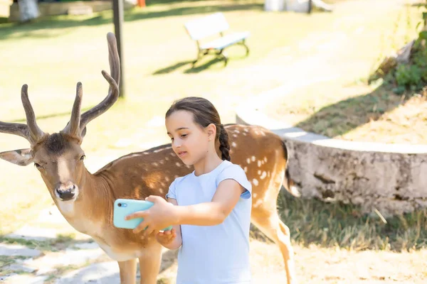 Küçük kız bir geyikle selfie çekiyor.