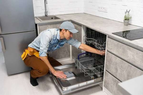 Genç yetişkin adam boşalıyor, yükleniyor. Ev işleri, modern mutfak gereçleri. Açık bir bulaşık makinesi. — Stok fotoğraf