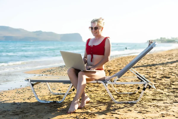 Όμορφη γυναίκα των επιχειρήσεων που εργάζονται σε απευθείας σύνδεση σε φορητό υπολογιστή, ενώ βρίσκεται στην παραλία Lounger. Freelancer κορίτσι χαλαρώνοντας και χρησιμοποιώντας Notebook εργασίας στο Διαδίκτυο. Τεχνολογία επικοινωνιών. — Φωτογραφία Αρχείου