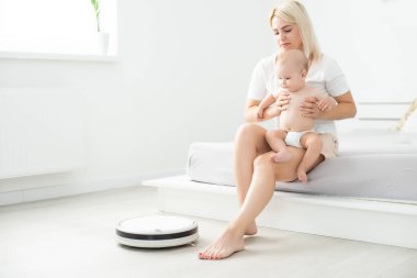 Bebeğin yanında robot süpürge var.