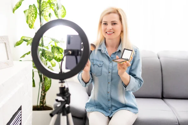 Blogger mujer grabando vídeo en smartphone e iluminándose con la lámpara de anillo en la mesa en la sala de luz — Foto de Stock