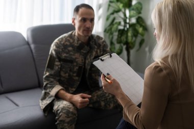 Psikologla terapi seansı sırasında koltukta oturan depresif bir asker.