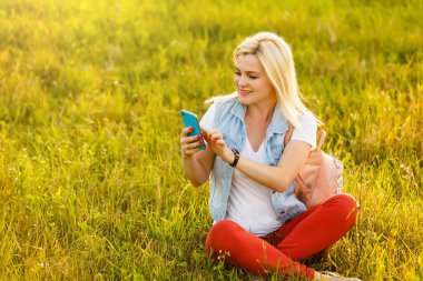 Parkta vakit, bir çim üzerinde oturan, dizüstü bilgisayar kullanarak, cep telefonu tutan genç ve güzel kadın
