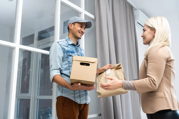 Zufriedener Zusteller, der Pakete trägt, während er seinen Kunden nach Hause liefert. — Stockfoto