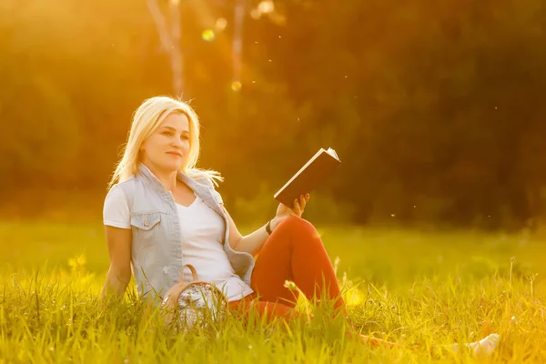 Contra o fundo de grama prado verde sentou-se jovem, menina encantadora, estudante lê livro — Fotografia de Stock