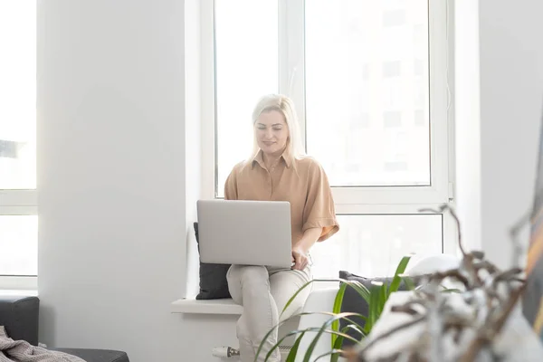 Sorrindo jovem usando laptop, sentado no sofá em casa, linda garota fazendo compras ou conversando on-line em rede social, se divertindo, assistindo filme, freelancer trabalhando no projeto de computador . — Fotografia de Stock