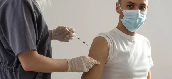 Kvinnlig läkare i handskar håller sprutan med vaccin läkemedel gör sig redo göra vaccination injektion från covid-19 coronavirus till sjuka arab latinamerikansk man patient i medicinsk mask på nära håll — Stockfoto