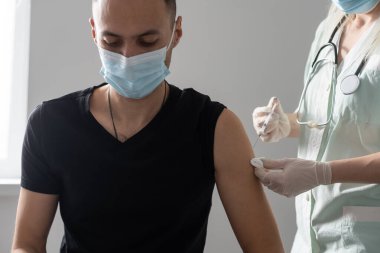 Eldivenli kadın doktor şırıngayla aşı ilacı hazırlıyor. Kovid-19 koronavirüsünden hasta Arap İspanyol maskeli hastaya aşı yapın. Kapatın.