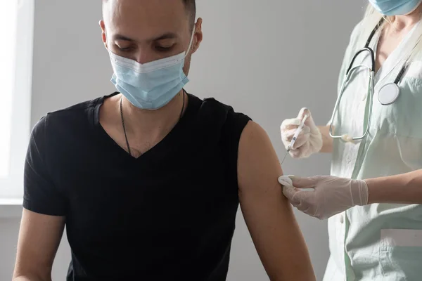 Femme médecin dans des gants tient seringue avec vaccin médicament se prépare faire injection de vaccin de covide-19 coronavirus à malade arabe hispanique homme patient en masque médical de près — Photo
