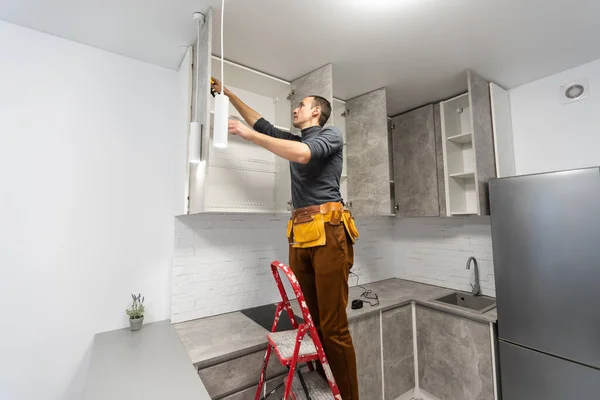 Konzeptualisierung der Deckenlampe im Raum. Ein glücklicher Mann auf einer Leiter zeigt zur Decke. — Stockfoto