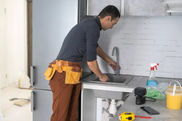 Lächelnder Handwerker, Tischler in Overalls, der in die Kamera lächelt, während er Küchenmöbel installiert — Stockfoto