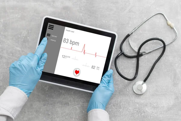 Doctor hand holding tablet with blank screen and stethoscope on grey table, copy space, top view — Stock Photo, Image