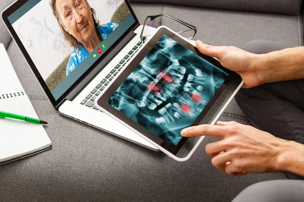 Обсуждение вопросов. Обрезанный снимок профессионального стоматолога, показывающего челюсти и рентгеновские снимки зубов пациенту с помощью цифрового планшета — стоковое фото