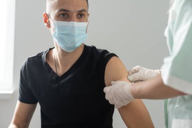 Eldivenli kadın doktor şırıngayla aşı ilacı hazırlıyor. Kovid-19 koronavirüsünden hasta Arap İspanyol maskeli hastaya aşı yapın. Kapatın.