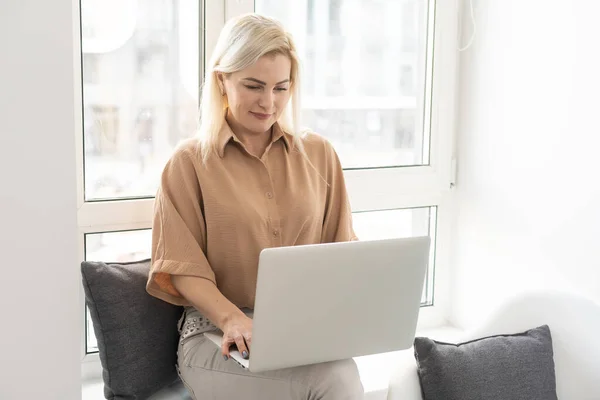 Élvezem az otthon töltött időt. Gyönyörű fiatal mosolygós nő dolgozik laptop otthon — Stock Fotó