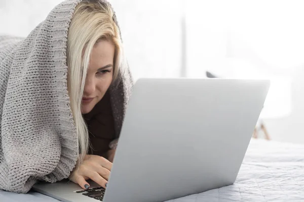 Kvinna med laptop täckt med filt i sovrummet — Stockfoto